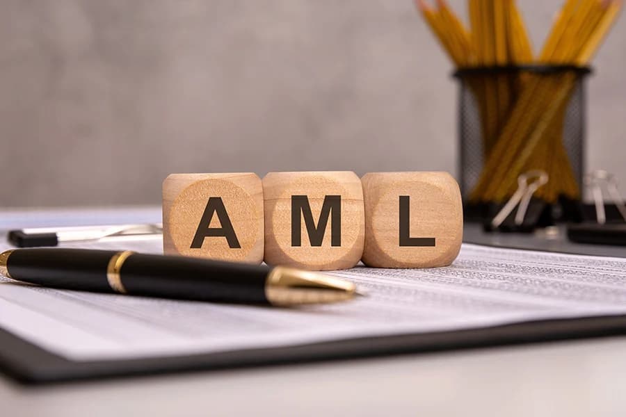 The letters AML on small wooden cubes placed on a clipboard next to a pen