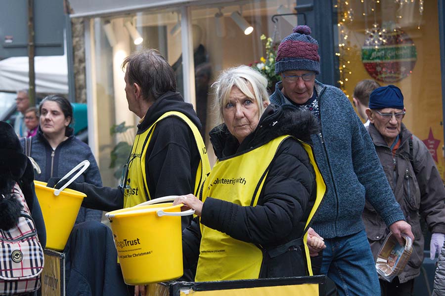 A female volunteer holds a charity collection bucket on a busy street