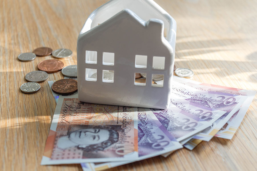 A small ceramic house on top of a pile of cash