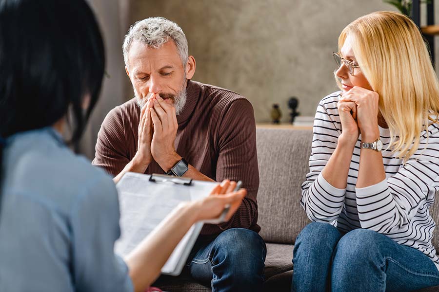 A woman holding papers speaks to a worried looking couple
