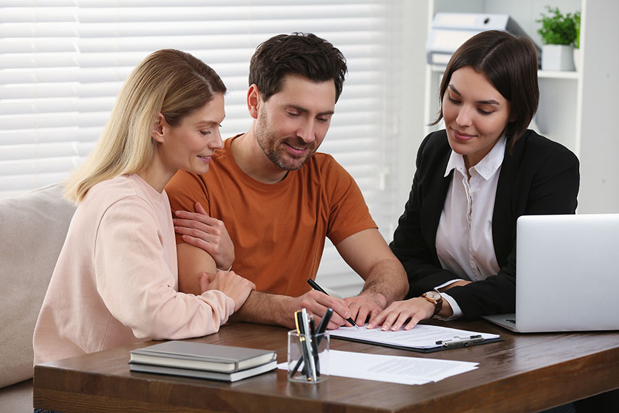 A young couple sign papers at a desk while a solicitor looks on