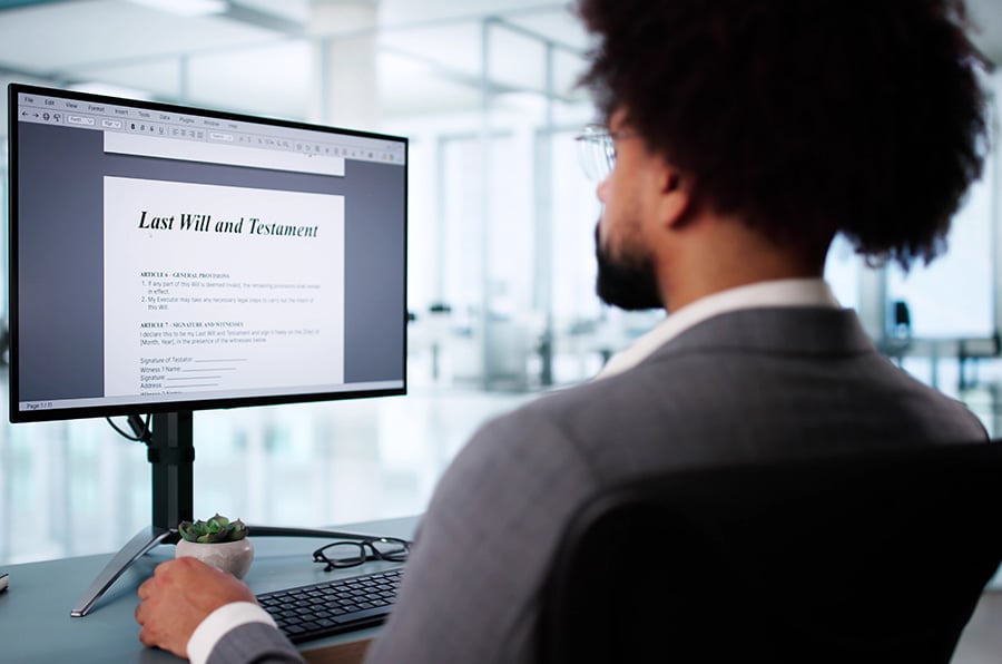 A man at a desk looks at a screen with the words 'last will and testament'