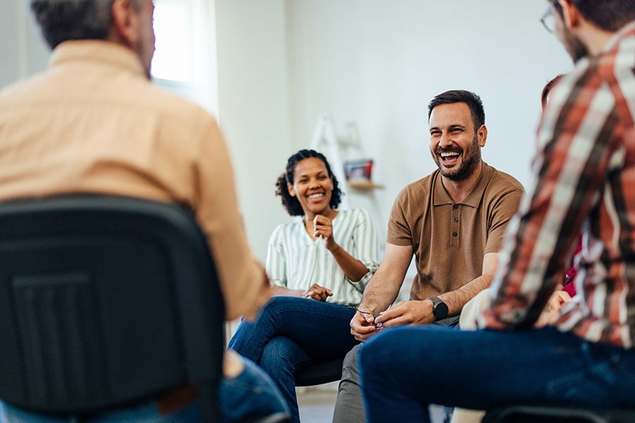 A group of smiling people sitting on chairs placed in a circle