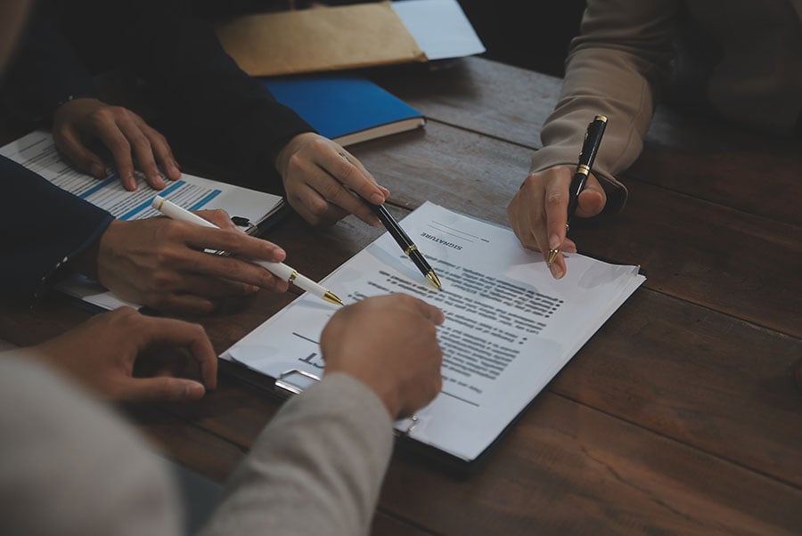 A close up of hands holding fountain pens signing papers on a table