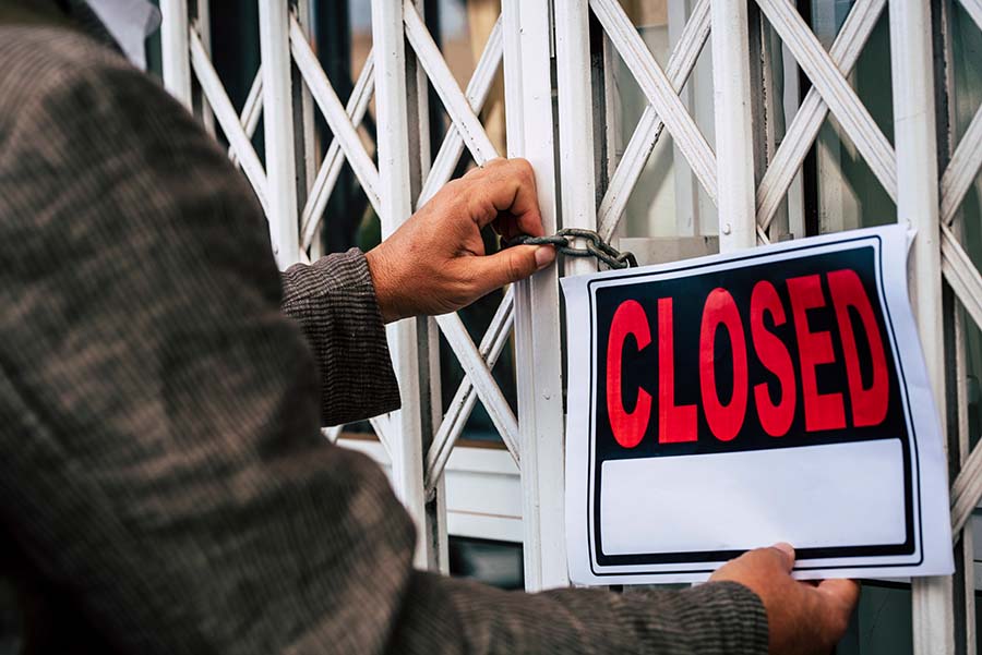 A man puts a closed sign across metal shutters closed with a padlock