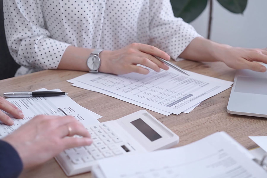A close up of two people working at a table surrounded by spreadsheets
