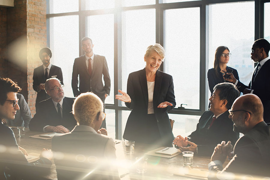 A group of around 15 people in suits meeting in a large boardroom