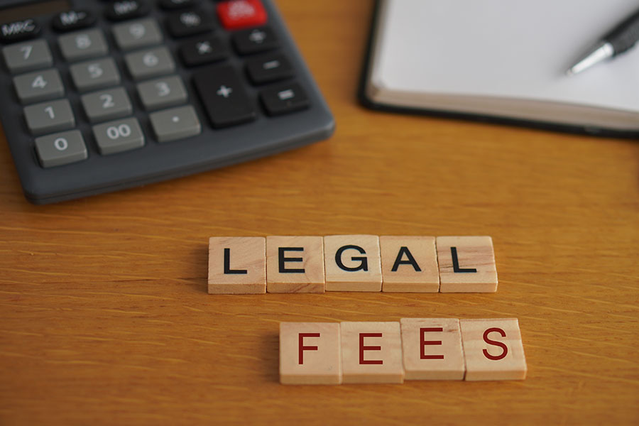 Tiles spelling out 'legal fees' next to a calculator and notepad and pen on a desk