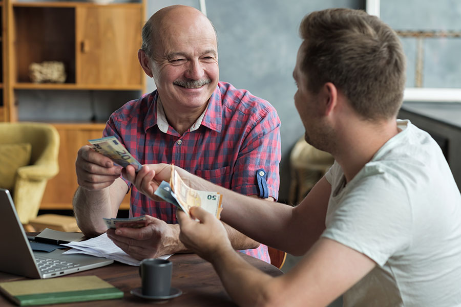 An older man hands a wad of cash to a younger man