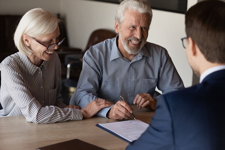A smiling older couple sign papers with a man in a suit
