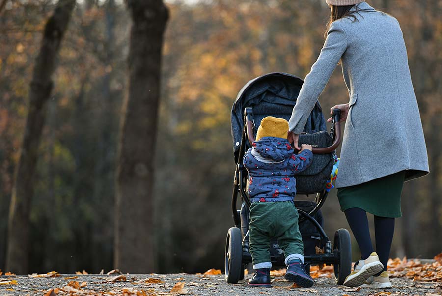 A woman with a small toddler pushes a pushchair outdoors