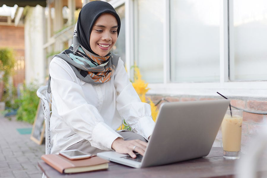 A smiling woman works on a laptop outside a cafe