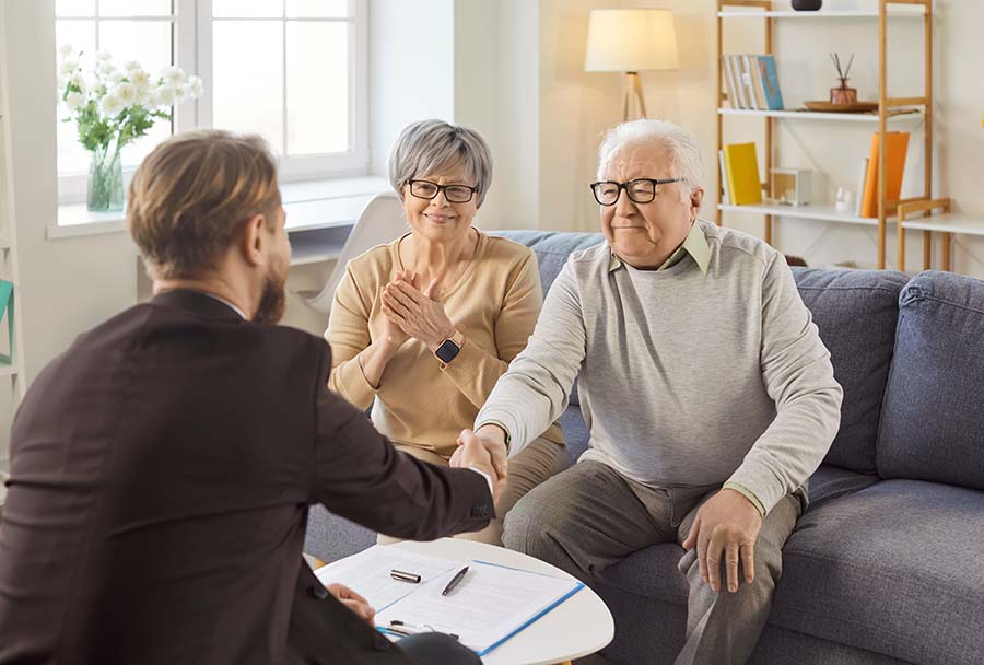 An elderly couple shake hands with a solicitor, with a pile of signed papers in front of them