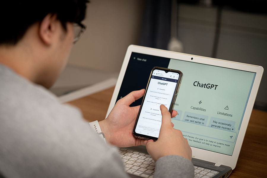 A man using a phone and a laptop, both with ChatGPT open on the screen