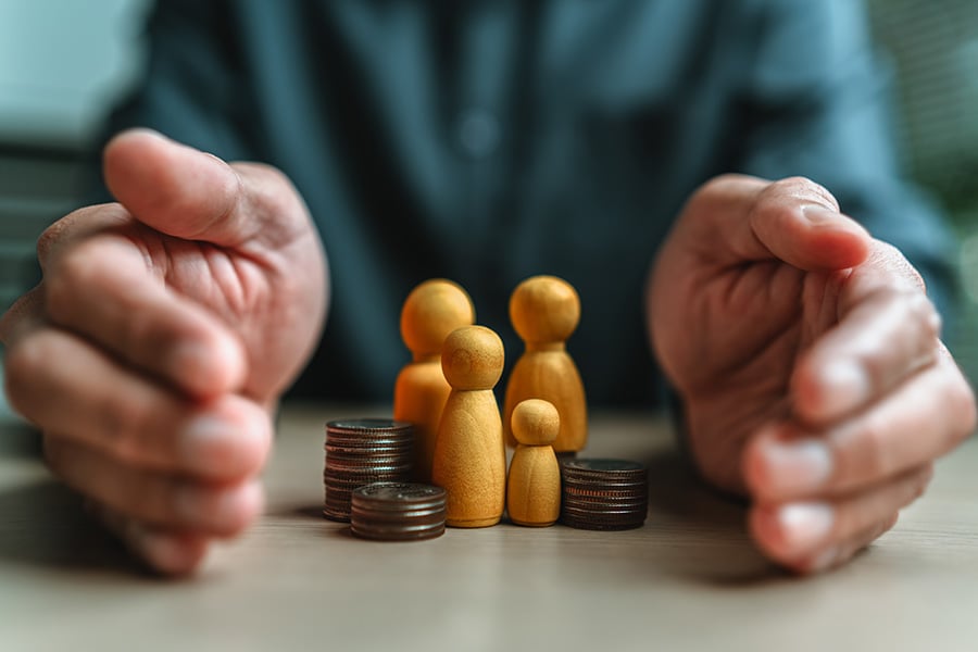 A man places hands protectively around four small wooden figures and a pile of coins