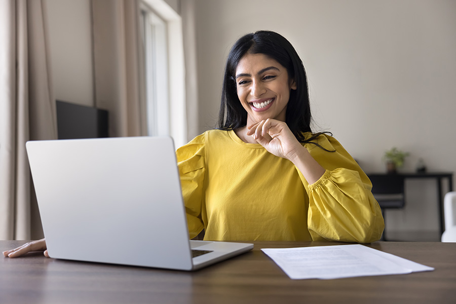 A smiling professional woman works on a laptop in an office