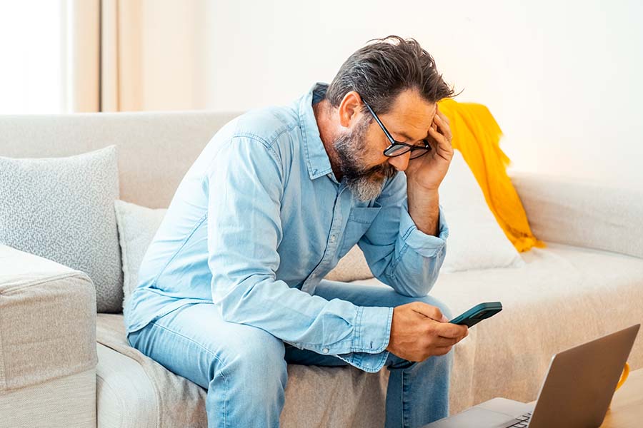 A stressed looking man using his phone with a laptop in front of him