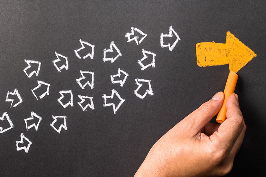 Lots of small white arrows grouped together, pointing to one large orange arrow, all drawn in chalk against a black background