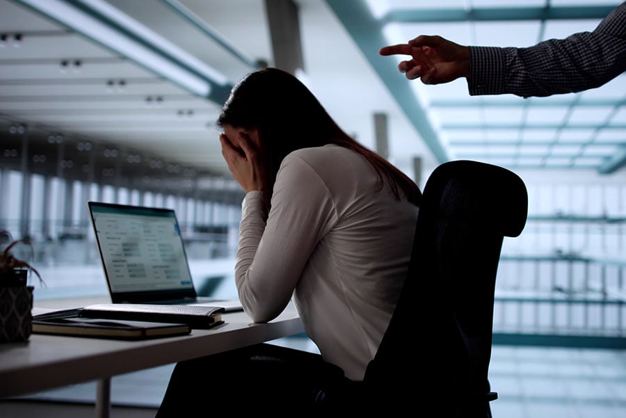A bullied woman at her desk in the office with an angry point pointing at her
