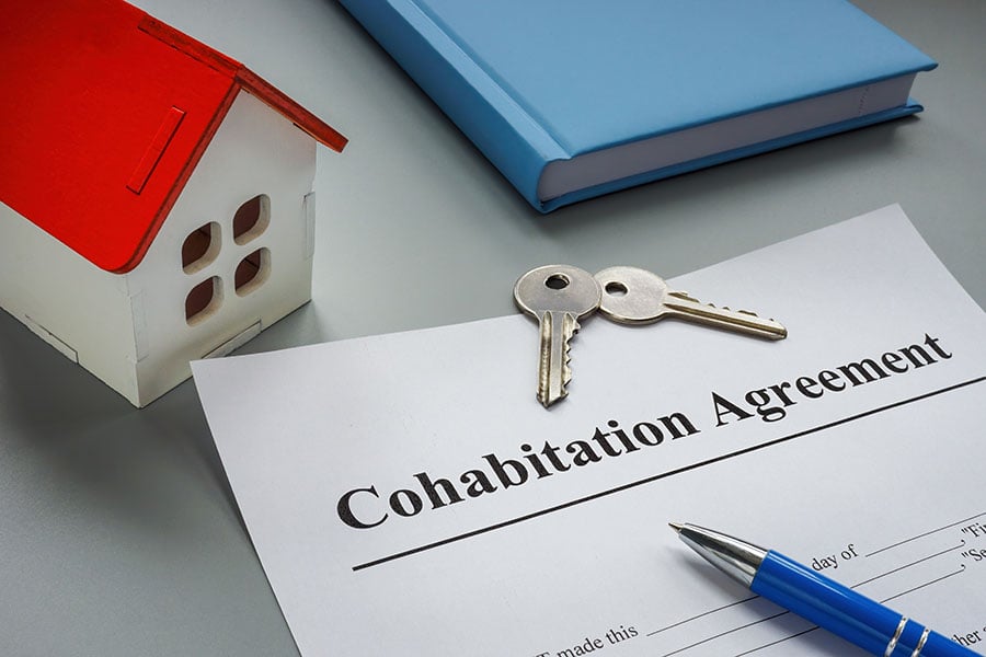 A cohabitation agreement with two house keys on top, next to a small toy house and a book