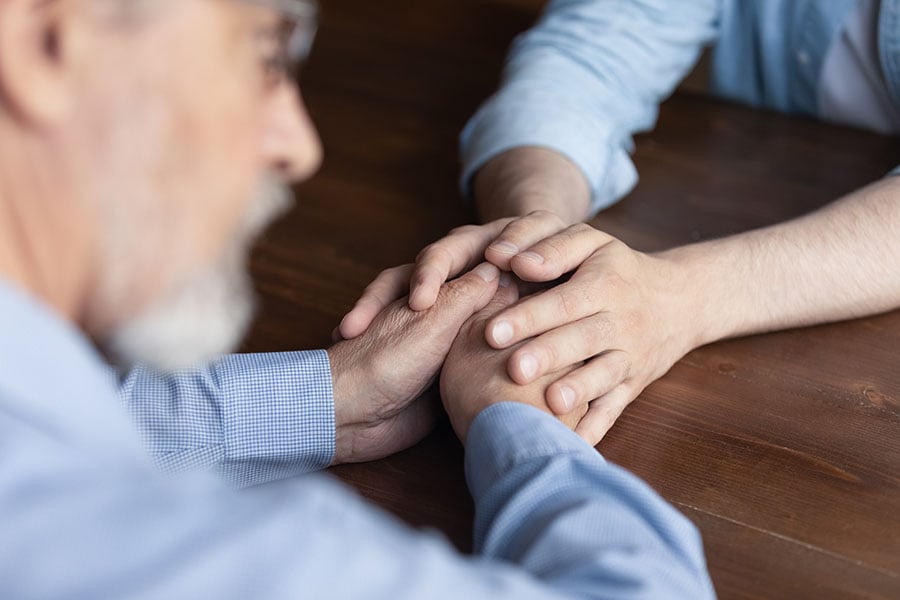 An out of focus close-up of a woman holding a mans hands over a table to comfort him