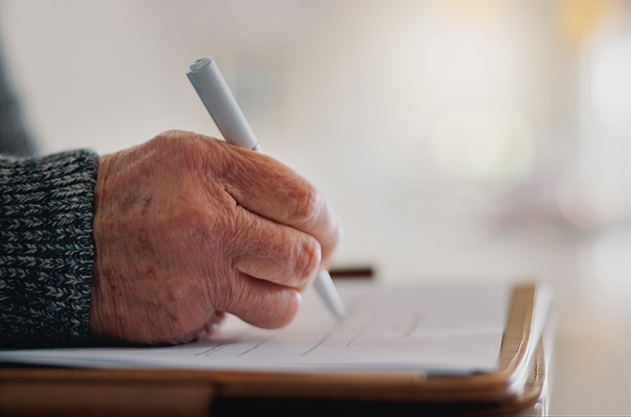 A close-up of an aged hand signing a will or document