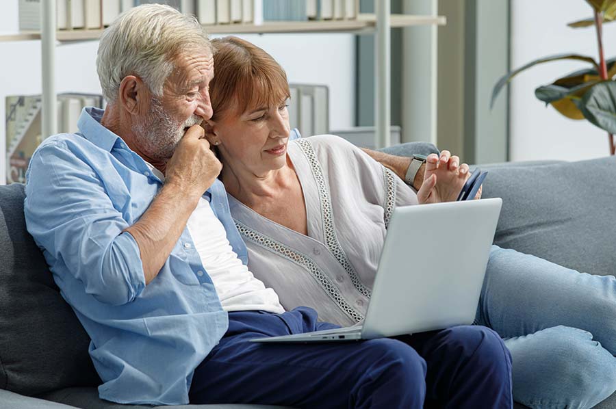 An older couple look at a laptop together while sitting comfortably on a sofa