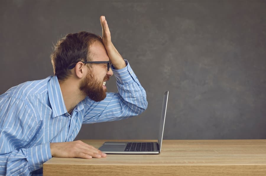 Argh, don't remember it. Side profile view angry ashamed guy slaps face sitting at office desk with laptop