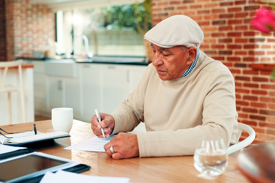 An elderly man sits at a table surrounded by paperwork