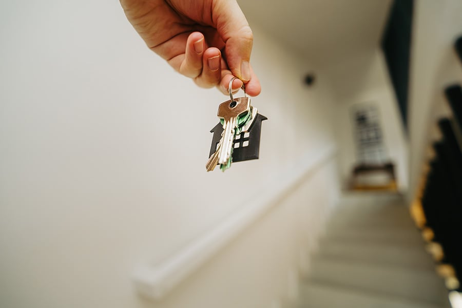 A close up of a hand holding a key with a house shaped keyring, while walking upstairs