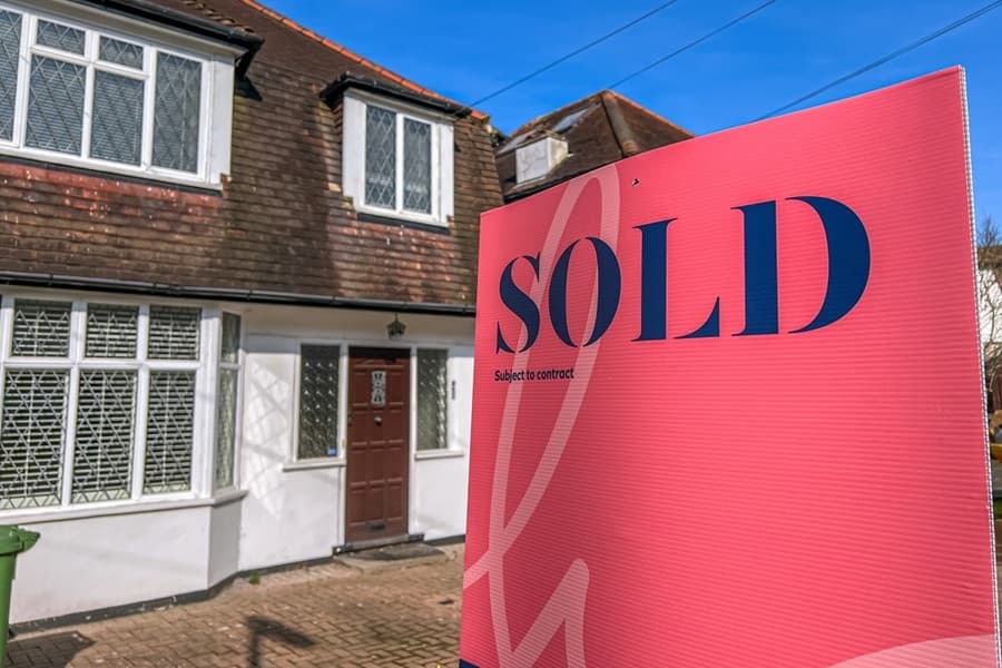 Estate agent SOLD sign with street of houses in background, London.