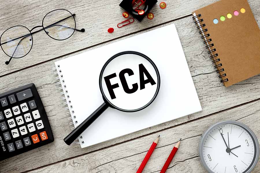 A table is laid out with a notepad with the letters FCA, a calculator, readign glasses, pencils and a clock