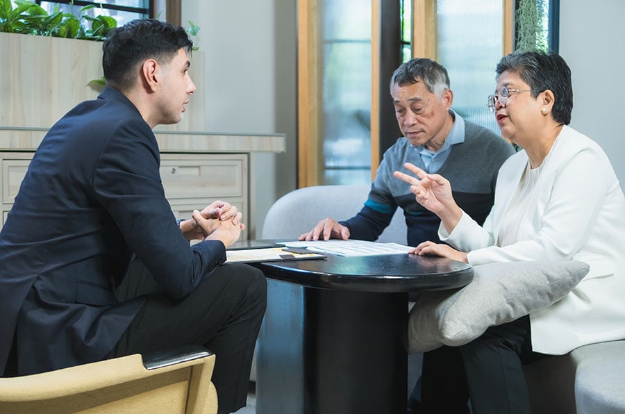 A financial adviser in conversation with an older couple, with papers on a desk in front of them