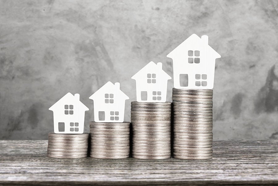 Small model white houses placed on top of increasingly large piles of coins