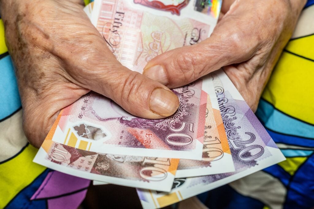 An old lady's hands holding a wad of £20 notes