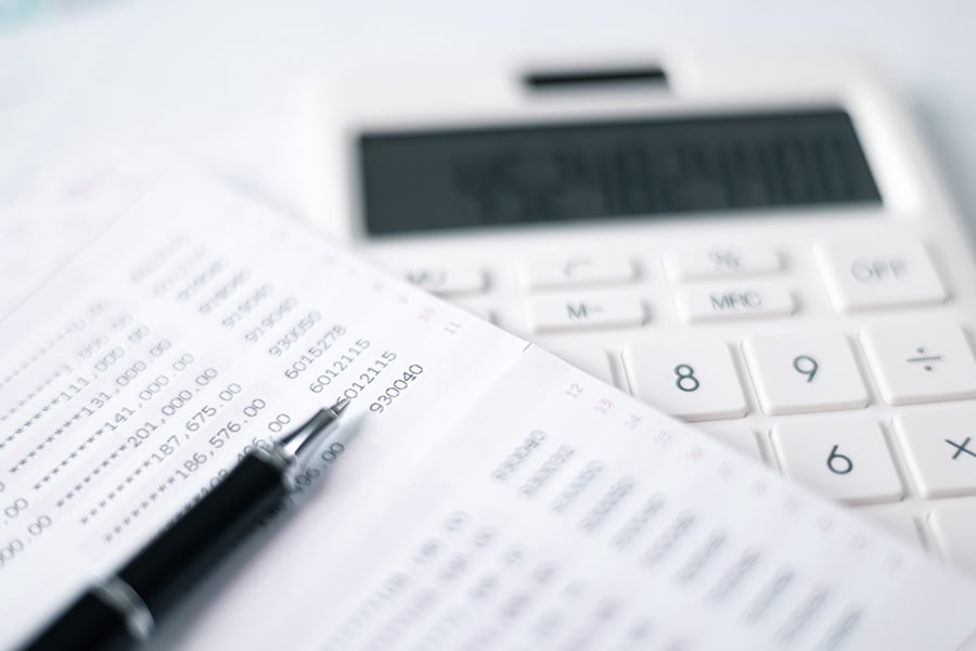 A spreadsheet on top of calculator with a fountain pen laid on the top