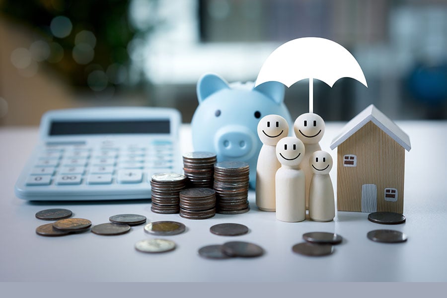 The image shows a calculator, piggy bank, piles of coins, a small house and small basic figures of people under an umbrella
